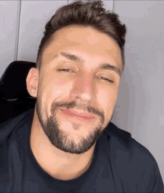 a man with a beard and a black shirt is smiling with his eyes closed