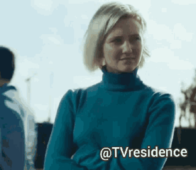 a woman wearing a blue turtleneck sweater is standing with her arms crossed and says @tvresidence