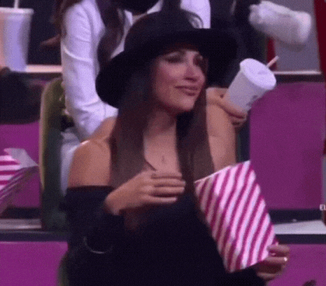 a woman in a hat is holding a bag of popcorn and a drink .