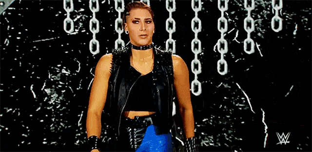 a woman in a leather vest and choker is standing in front of a wall with chains .