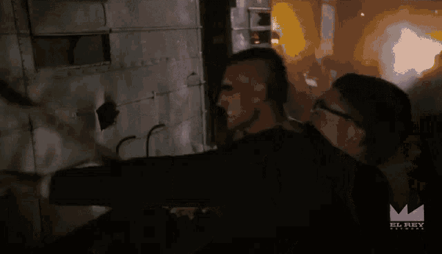 two men are standing next to each other in a dark room with the el rey network logo on the bottom right