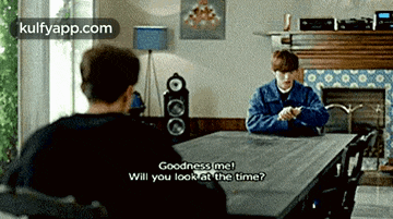 two men are sitting at a table and one of them is asking the other to look at the time .