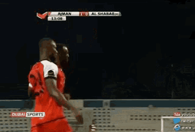 two soccer players are hugging each other on a field during a match sponsored by dubai sports