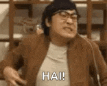 a man wearing glasses and a brown jacket is making a funny face and saying hai .
