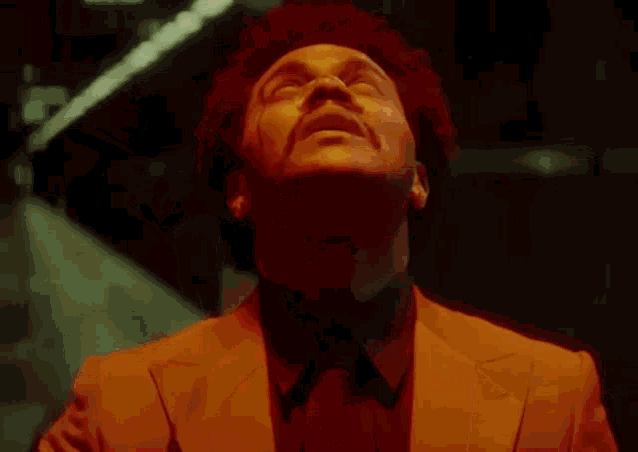 a man in a suit and tie is standing in a dark room looking up at the sky .