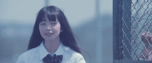 a girl in a white shirt and black bow tie is standing in front of a chain link fence