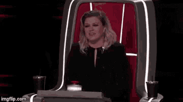 a woman is sitting in a chair holding a microphone and screaming .