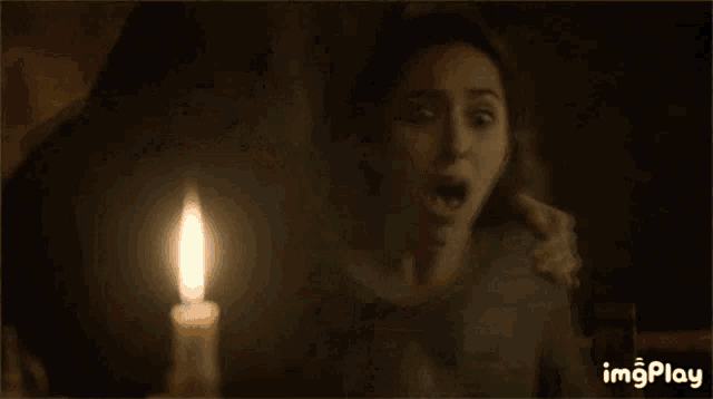 a woman is crying in front of a lit candle with imgplay written on the bottom right