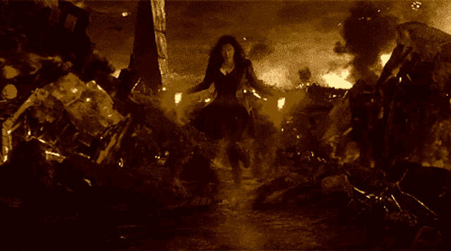 a woman in a black dress is standing in front of a pile of fire