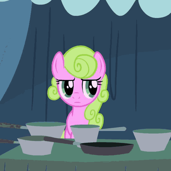 a pink pony with green hair is sitting at a table with pans