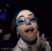 a woman wearing blue sunglasses and a white turtleneck is smiling and making a funny face .