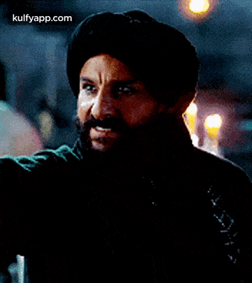 a man with a beard and mustache is wearing a turban and a black jacket .
