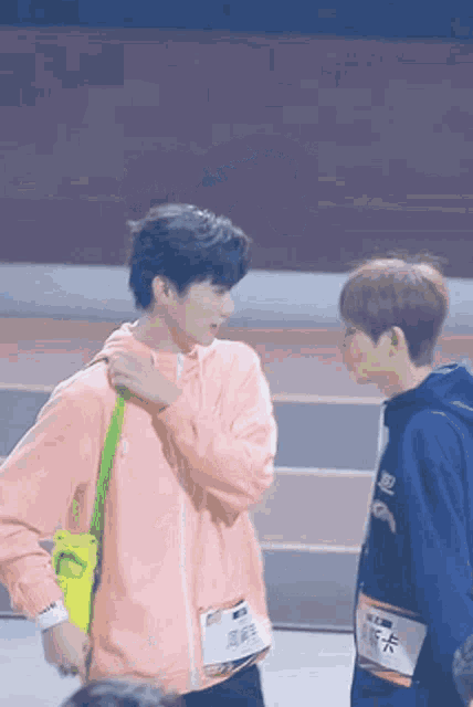 two young men are standing next to each other and one of them is wearing a pink hoodie .
