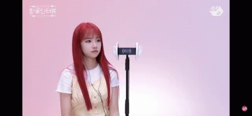 a girl with red hair is standing in front of a microphone on a pink background