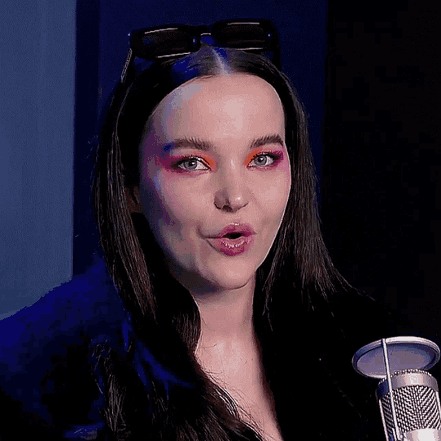 a woman with sunglasses on her head stands in front of a microphone with her mouth open