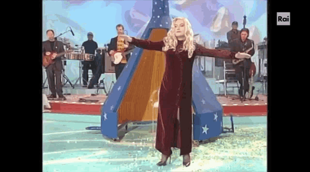 a woman in a red dress is standing in front of a stage with a band behind her and the letters rai on the bottom