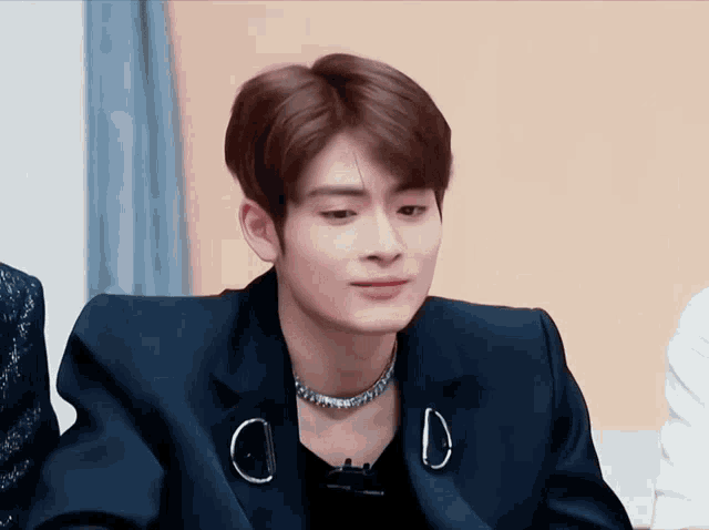 a young man wearing a black jacket and a necklace with the letter d on his chest