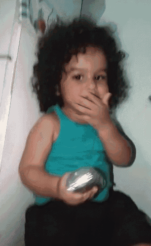 a little girl with curly hair covering her mouth while holding a silver object