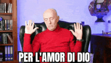 a bald man in a red sweater is sitting in a chair with his eyes closed and his hands up .