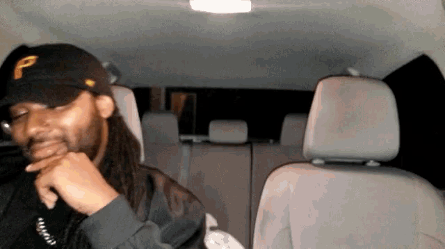 a man wearing a hat with the letter p on it sits in the back seat of a car