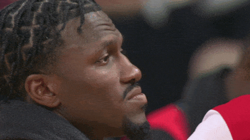 a man with braids in his hair wears a scarf around his neck