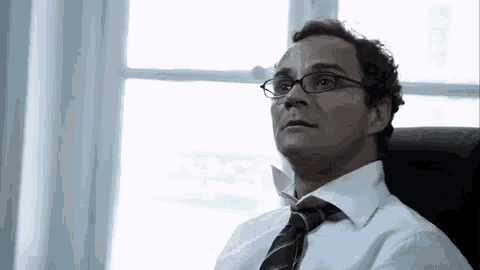 a man wearing glasses is sitting in a chair in front of a window .
