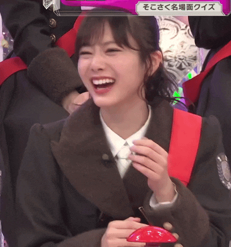 a girl in a suit is smiling and holding a red button in her hand