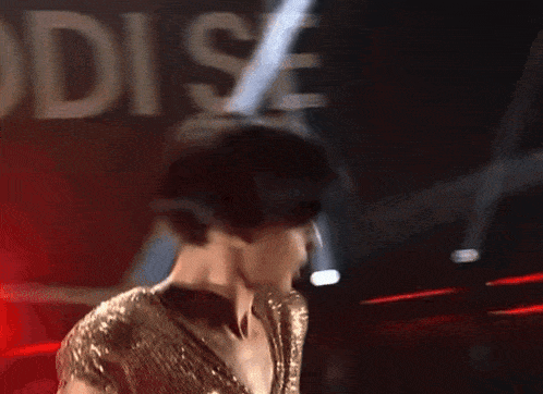 a man in a gold dress is dancing in front of a sign that says body