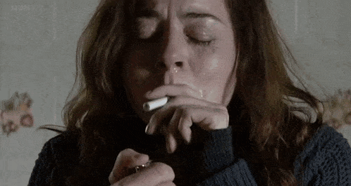 a woman is crying while smoking a cigarette in a dark room .