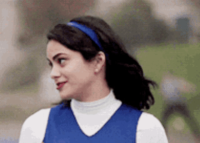 a woman wearing a blue headband and a white turtleneck is smiling and looking to the side .