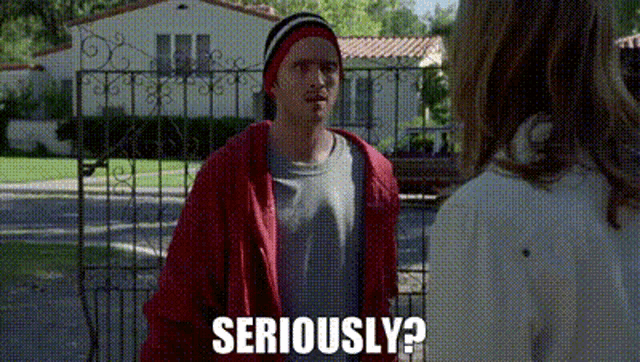 a man in a red jacket is standing next to a woman in front of a house and says `` seriously ? ''
