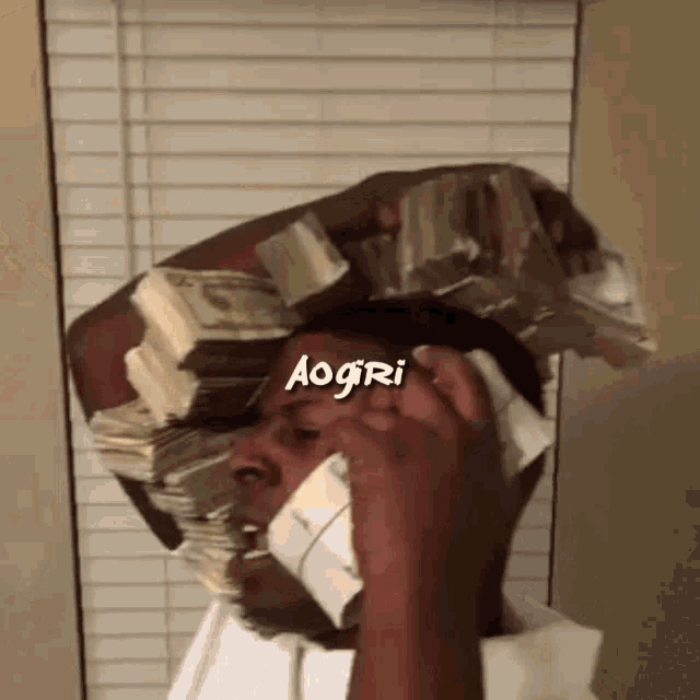 a man is talking on a cell phone while holding a pile of money on his head .