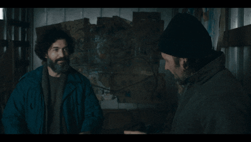 a man with a beard and a beanie is talking to another man