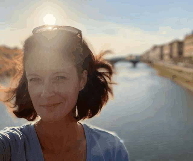 a woman wearing sunglasses stands in front of a river