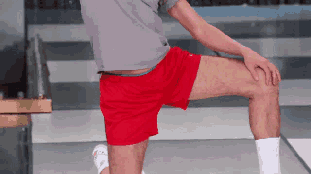 a man wearing red shorts and white socks stretches his legs