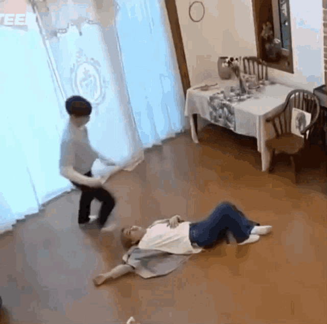 a man is laying on the floor in a living room while another man is standing in front of a table .