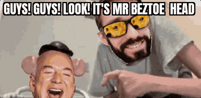 a man with a beard wearing sunglasses laughs next to another man