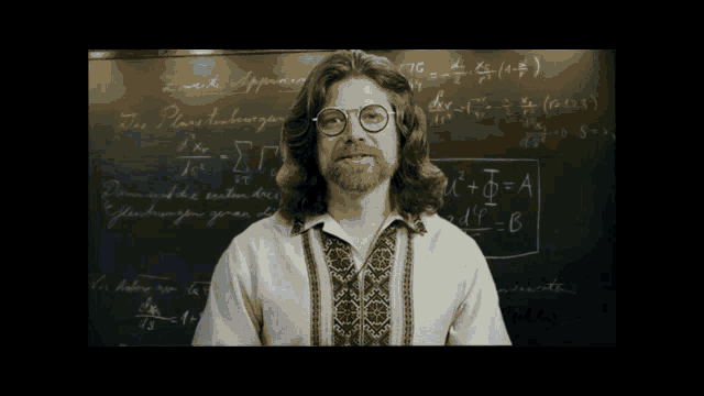 a man wearing glasses stands in front of a blackboard with equations written on it including one that says " equation "
