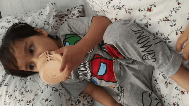 a little boy drinking from a bottle with the word among us on his shirt