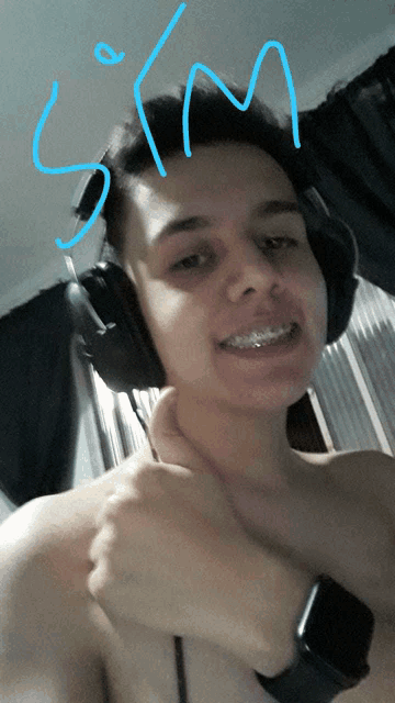 a shirtless man wearing headphones and a smart watch has the letter s on his forehead