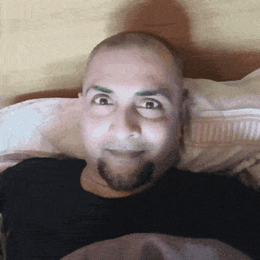 a man with a beard is smiling while laying on a pillow