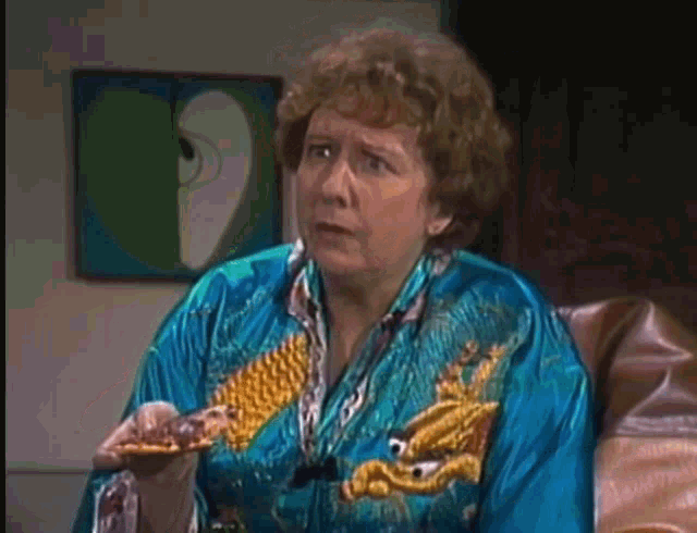 an elderly woman in a blue robe is sitting in a chair holding a piece of food .