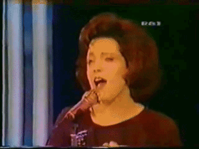 a woman singing into a microphone with the letters rt on the bottom left