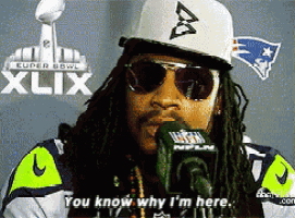 a man wearing sunglasses and a hat is talking into a microphone in front of a super bowl xlix poster