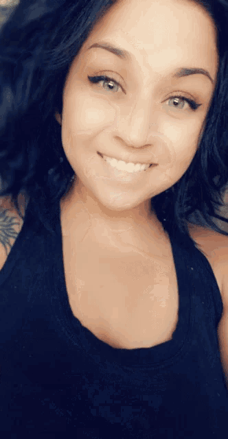a woman in a black tank top is smiling for the camera