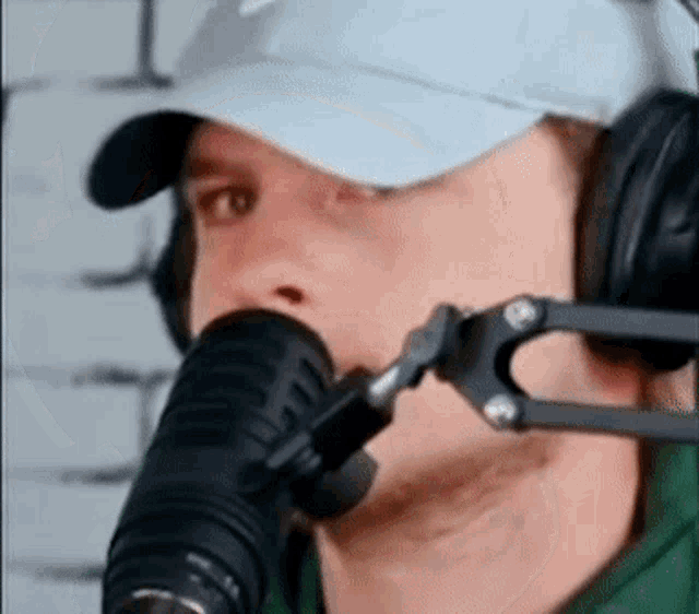 a man wearing a white hat and headphones is talking into a microphone .