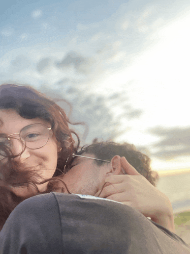 a woman with glasses is hugging a man with his head on her shoulder