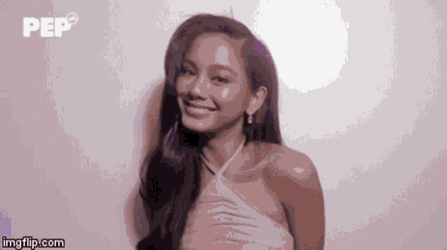a woman in a pink dress is smiling and looking at the camera while standing in front of a white wall .