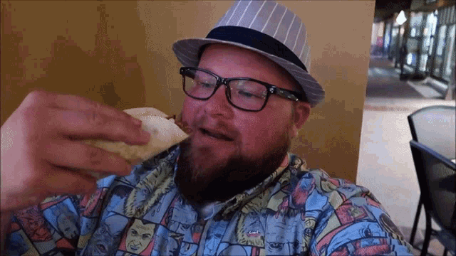 a man with glasses and a hat is eating a sandwich