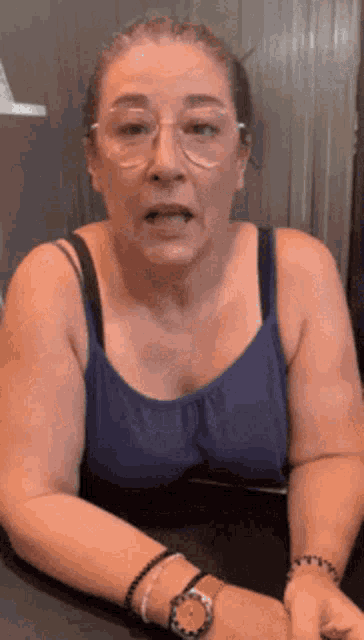 an older woman wearing glasses and a blue tank top
